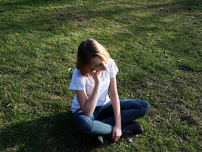 悲伤沉思的少女坐在公园的草地上