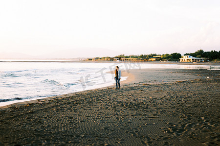 一件毛线衣的女孩沿海滩走并且看海浪