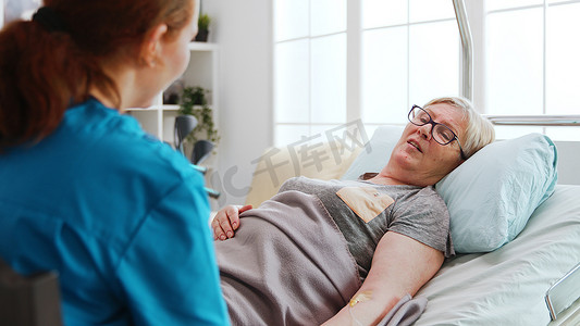 在疗养院，躺在床上的老病妇与一位女护士交谈