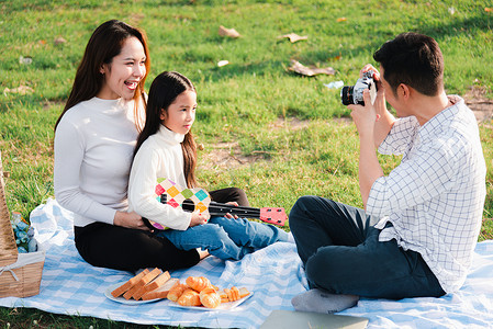 派对banner摄影照片_一家人的父亲、母亲和孩子一起玩乐，享受户外活动，坐在草地派对上拍照