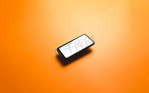 简约的模拟平面图像设计，带有带有复制空间和白色屏幕的浮动手机，可在平面橙色背景上书写