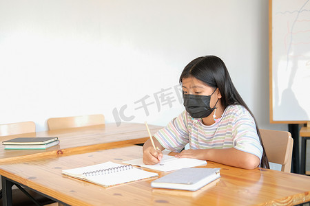 戴着口罩学习写笔记做作业的女学生。