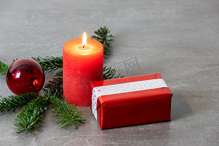 深灰色大理石背景上带有红色燃烧蜡烛、诺德曼冷杉树枝、红色圣诞树球和礼品包裹的圣诞主题