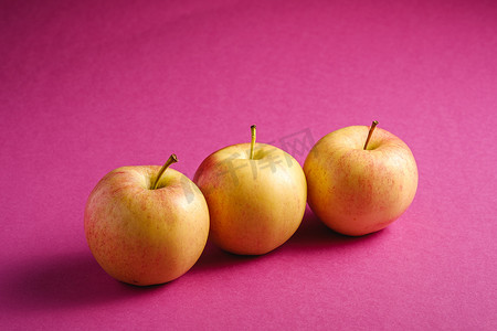 粉紫色纹理背景中鲜甜的三个苹果