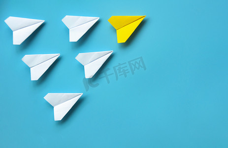 纸飞机的顶视图-黄色纸飞机折纸在蓝色背景上领先其他白色飞机。