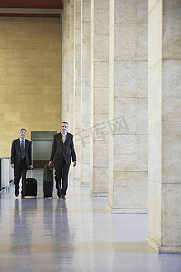 公司大厅摄影照片_两个微笑的商人在机场大厅拉着行李的全长