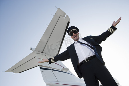 站立的男子摄影照片_快乐的机长双臂靠在机翼上站立的低视角