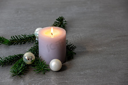 深灰色大理石背景上带有白色燃烧蜡烛、诺德曼冷杉树枝和银色圣诞树球的圣诞主题