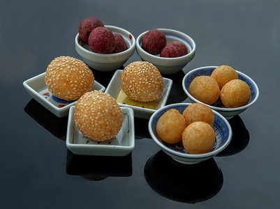 芝麻球摄影照片_黑桌上的芝麻炒甘薯球和深炸紫色和黄色甘薯球（鹌鹑糖蛋）。