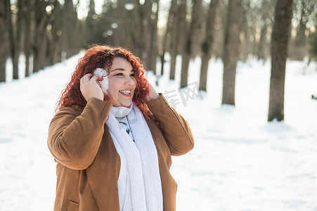 丰满摄影照片_一个丰满的女人冬天在公园散步时戴着耳机听音乐。