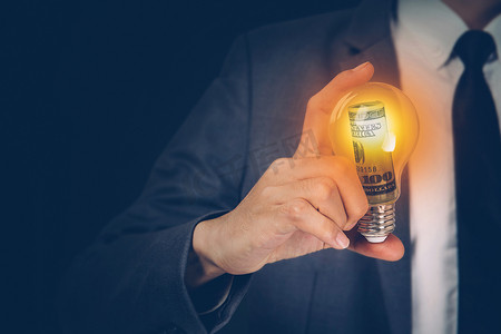 发光灯泡摄影照片_手持灯泡的商人的手有货币美元、金融的成功、创新和能源、规划与财务储蓄、远见和知识、灯泡发光、商业理念。