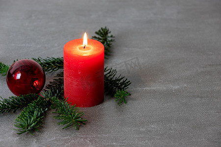 免费圣诞摄影照片_深灰色大理石背景上带有红色燃烧蜡烛、诺德曼冷杉树枝和红色圣诞树球的圣诞主题