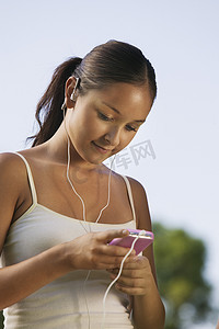 音乐的播放器摄影照片_年轻女子在户外听便携式音乐播放器。