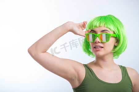 戴着绿色假发和滑稽眼镜的快乐年轻女性在白色背景下庆祝圣帕特里克节