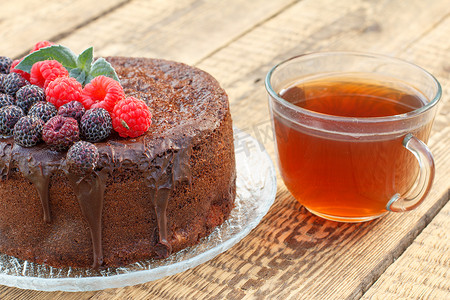 自制巧克力蛋糕在玻璃板上装饰着黑色和红色的覆盆子，还有一杯茶。