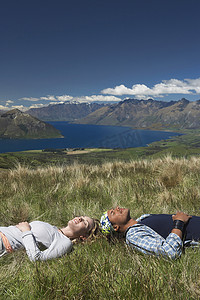 一男一女躺在田野里俯瞰山湖的侧视图