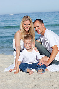 快乐的父母和他们的儿子坐在沙滩上的肖像