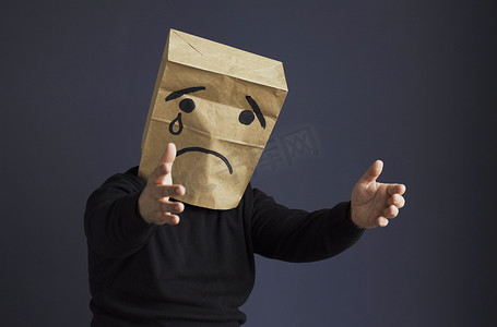 悲伤的男人头上顶着一个袋子，画着哭泣的表情符号。