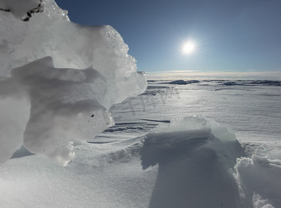 蓝色结晶摄影照片_阳光明媚的冬日冰坡，蓝色透明的冰，纯蓝的天空，长长的阴影，纯净的积雪覆盖的处女地，雪地，