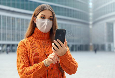 在现代城市街道上使用智能手机应用程序戴口罩的年轻女性。