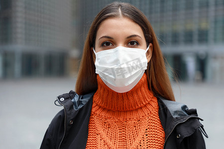 戴着医用口罩的年轻女性站在空荡荡的现代城市街道上，看着准备接种疫苗的相机