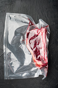生鲜肉摄影照片_真空市场包装中的生鲜肉俱乐部牛排，黑石背景，顶视图平躺