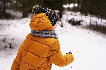 一个穿着黄色羽绒服和帽子的孩子冬天在森林里散步
