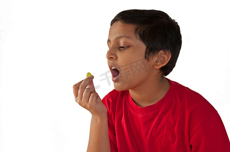 “小男孩吃葡萄，张开嘴，孤立在白色背景上”