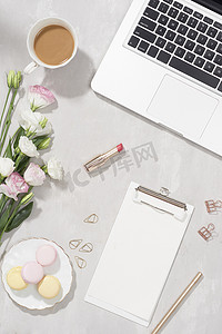女性平躺式工作区，白桌上放着笔记本电脑、一杯茶、马卡龙、口红和鲜花。