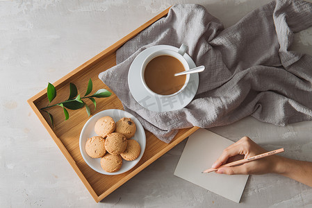 茶手写摄影照片_男性手在石桌上写明信片，端着一杯咖啡和饼干。