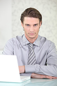 打领带的男人摄影照片_穿衬衫打领带的男人坐在笔记本电脑前