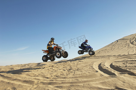 摩托车摄影照片_两名男子在沙漠中骑四轮摩托车的侧视图