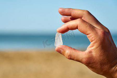 一个人的手指和拇指之间夹着一块白色的海玻璃