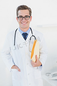 拿着文件夹的微笑的年轻医生看照相机