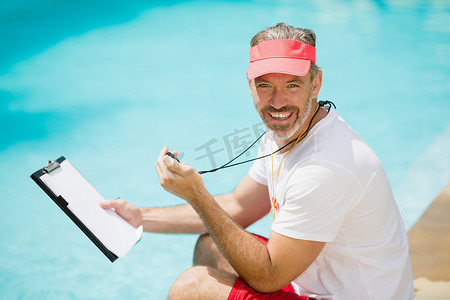 健身游泳教练摄影照片_游泳教练在泳池边拿着秒表和剪贴板的画像
