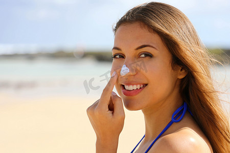特写年轻漂亮的女人在海滩上的鼻子上涂抹防晒霜。