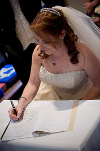 美丽的红发新娘用黑笔在婚礼登记簿上签字
