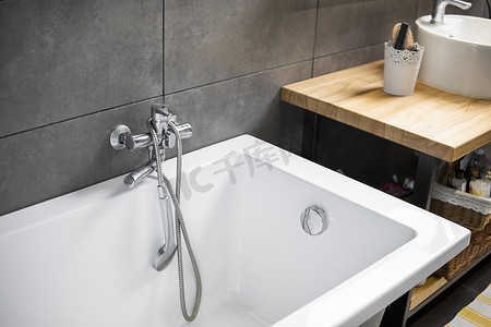 浴室内部墙上贴着灰色瓷砖，时尚的白色浴缸配有银色水龙头。
