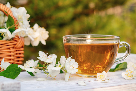 夏天在户外白色木盘上放着茉莉花茶的花和花瓣，在某个地方叫做茉莉花或假橙子，还有一杯香茉莉花茶