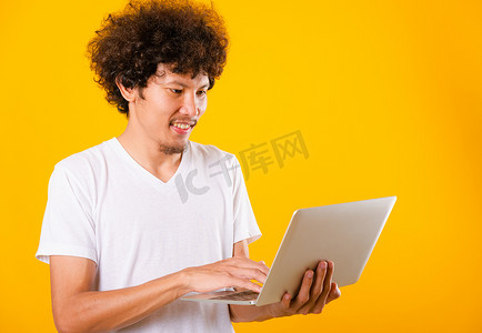亚洲帅哥摄影照片_一头卷发的亚洲帅哥使用笔记本电脑隔离