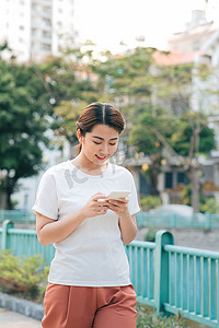 在公园里手持智能手机阅读短信的迷人亚洲女孩