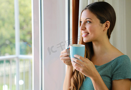 透过窗户在家喝咖啡的美女画像，专注于模特眼睛，室内拍摄