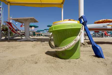 沙滩阳光摄影照片_“阳光明媚的日子里，儿童沙滩玩具桶、铲子和铲子在沙滩上”