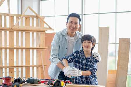 亚洲父亲和男孩拿着木工电钻，面带微笑地看着镜头。