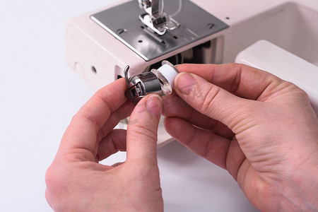 缝纫机特写摄影照片_裁缝将 babine 插入缝纫机的金属线轴架中。
