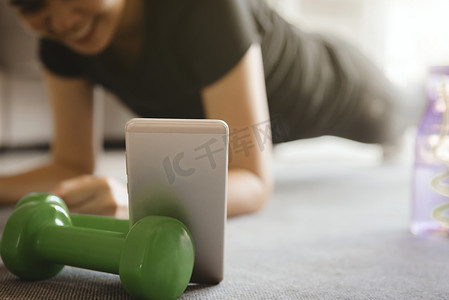 健身房全景摄影照片_一位运动型女性在家中客厅锻炼时使用智能手机。