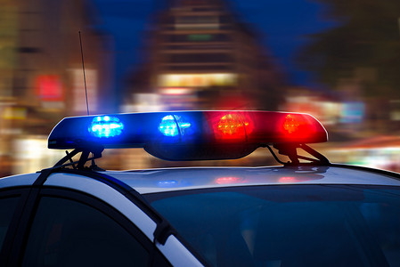 逮捕摄影照片_夜城街道上闪烁着蓝色和红色灯光的警车。