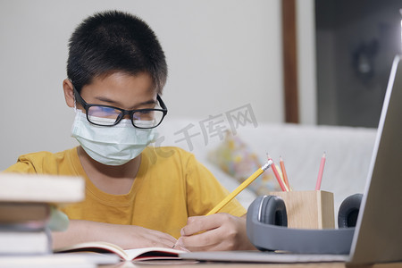 男孩戴着口罩在家上网学习。