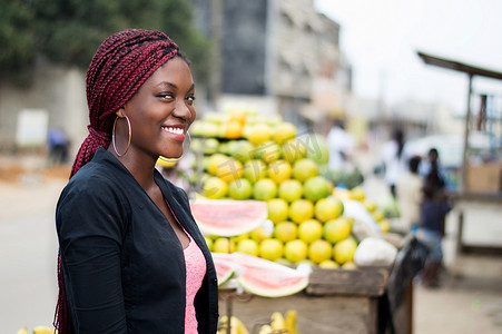 微笑的年轻女子站在水果货架旁的画像。