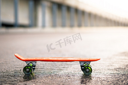 雨中湿路上橙色滑板的特写